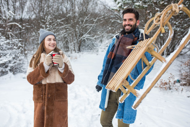 一对年轻夫妇在玩雪球、玩雪橇、喝热饮，享受初雪图片下载