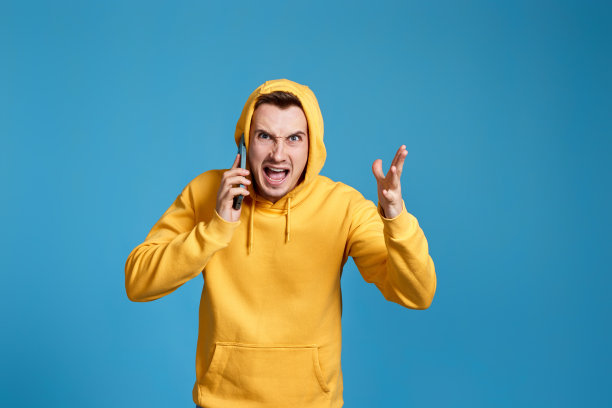 身穿黄色运动衫的愤怒男子手持手机图片下载