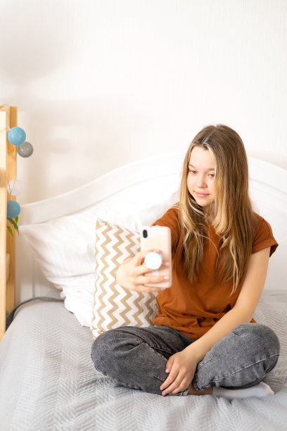 美丽的白人少女在家里用她的智能手机自拍，微笑，有乐趣，欣赏自己。图片下载