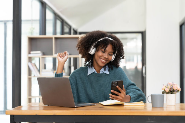 欢快快乐的混血女性在家玩游戏，戴着无线耳机的照片，在智能手机上玩游戏，赢得胜利的时刻。有趣又愉快的假期图片下载