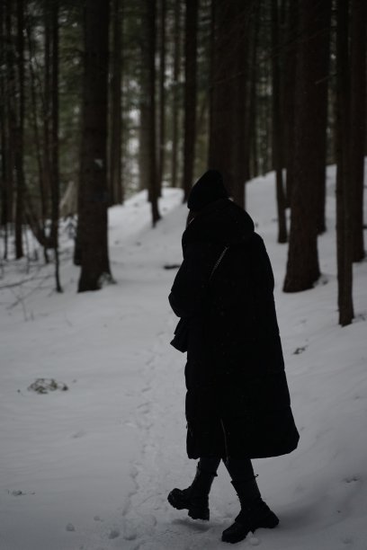 垂直拍摄一名穿着黑色冬季夹克的女性走在森林里的雪道上图片下载