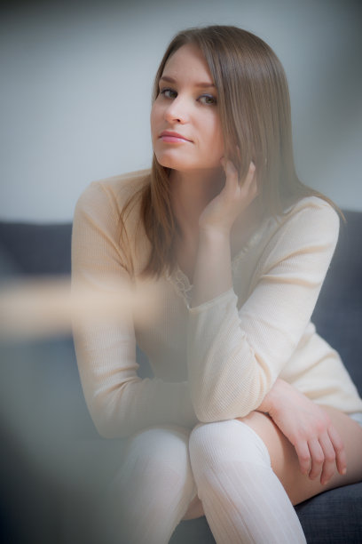 年轻的黑发美女肖像坐在沙发上，穿着白色的高丝袜。图片下载