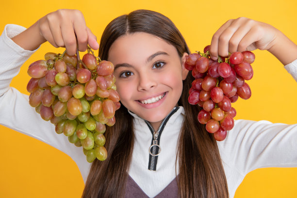 快乐的孩子与葡萄串在黄色背景图片下载