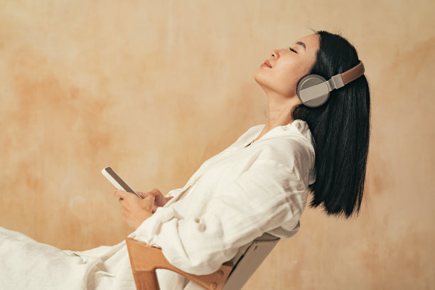 侧视图的妇女享受音乐无线耳机靠在椅子上，拿着手机图片下载