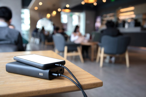 使用电源银行为手机充电，前面模糊的咖啡馆背景图片下载