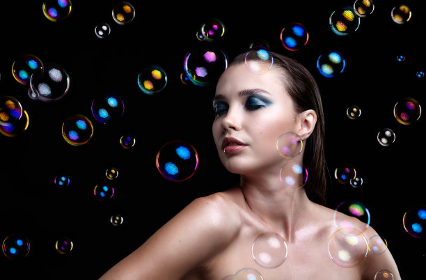 漂亮的年轻黑发女人，黑色背景上有肥皂泡图片下载