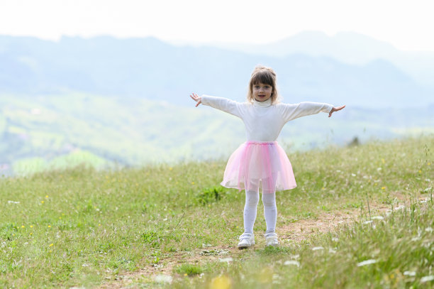 有山景的草地上的小女孩。张开双臂，快乐的小女孩在徒步旅行时玩得很开心。图片下载