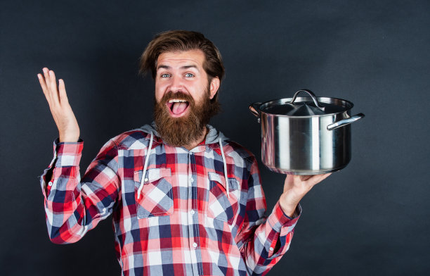 时髦的大胡子男子与时髦的发型穿格子衬衫hold锅，餐厅图片下载