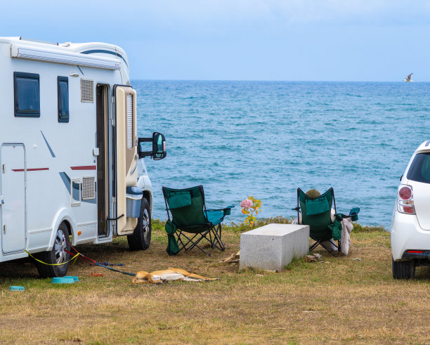 房车的背景是大海，还有两把能看到海景的椅子。游客在椅子上休息，旁边是他拴着皮带的狗。一只海鸥飞向地平线。图片下载