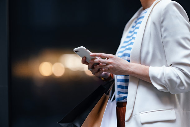 近距离拍摄的女子双手在户外使用手机和拿着购物袋图片下载