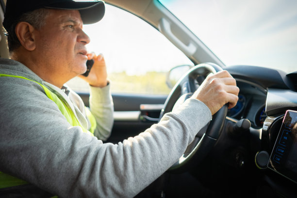 成熟的快递员一边开卡车一边用智能手机交流。图片下载