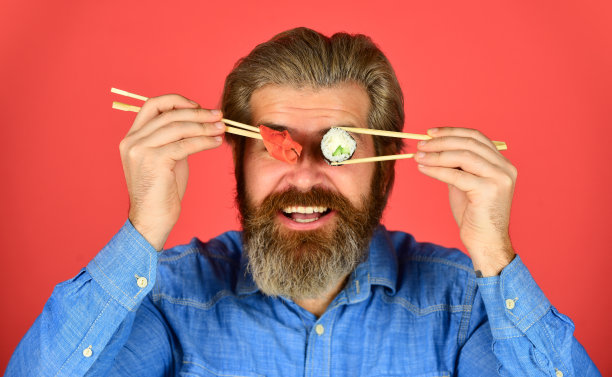 男人吃寿司筷子。日本料理。亚洲餐。寿司卷。寿司卷。东方文化。大胡子潮人吃面包卷。日式外卖。与寿司或生鱼片一起食用的腌姜图片下载