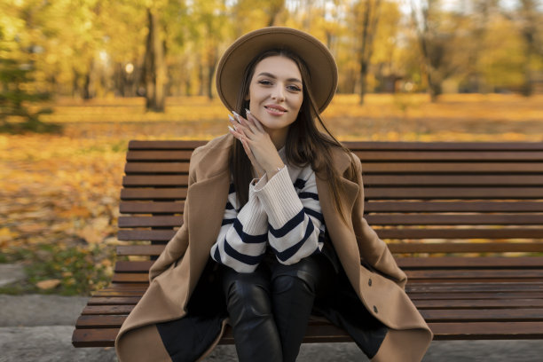 迷人的时尚微笑肖像迷人的时尚微笑女子长发散步在公园里，穿着温暖的棕色外套秋天时髦的时尚，戴着街头风格的帽子图片下载