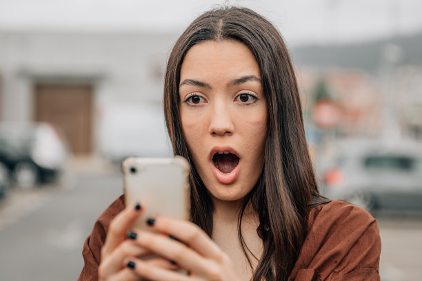 女孩在街上拿着手机，表情惊讶图片下载