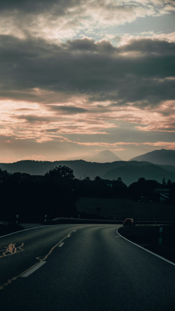 在巴伐利亚的Konigssee，一条垂直的柏油路背对着日落时分被森林覆盖的山脉图片下载