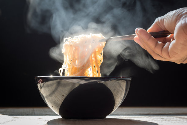 手用筷子夹起有蒸汽和烟雾的美味面条在碗上的木制背景，选择性聚焦图片下载