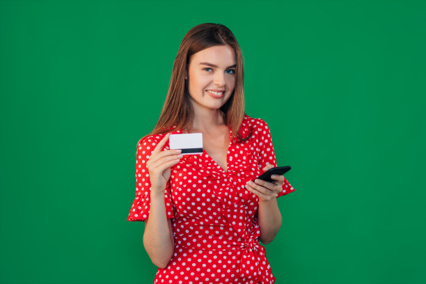 微笑的女孩拿着智能手机和信用卡。在绿色背景上穿着便服的女孩。情感的概念和愉悦的感受，购物。图片下载