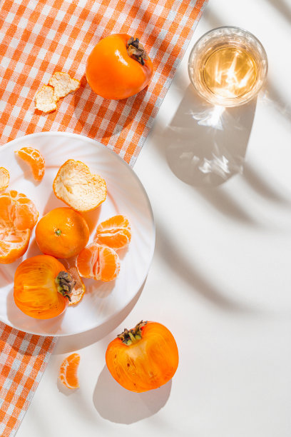 由新鲜的橘子，柿子和一杯饮料在白色背景与棕榈树叶阴影的创意组成。健康食品的概念。夏日野餐的主意。图片下载