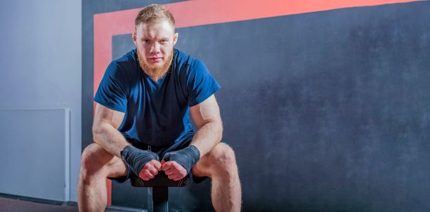 年轻的大胡子综合格斗选手坐在沙发上，准备战斗。看着镜头。图片下载