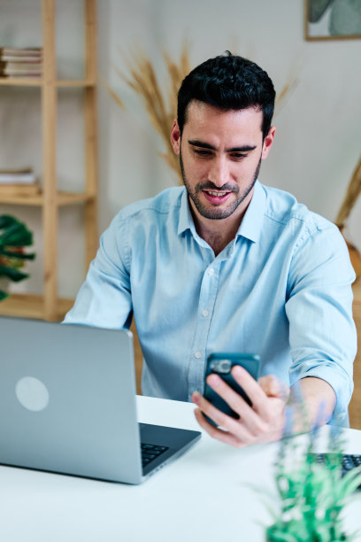 快乐的男人在家里使用智能手机和笔记本电脑图片下载