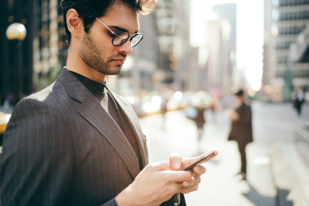 时髦的年轻商人穿着正装站在大城市的市中心用智能手机通过4G网络上网聊天，成功的律师在街上用手机打字图片下载