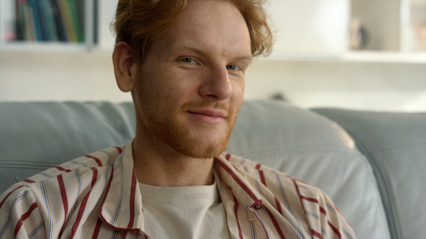 快乐的潮人在家里休息沙发特写。微笑的姜黄色男人靠在沙发上图片下载