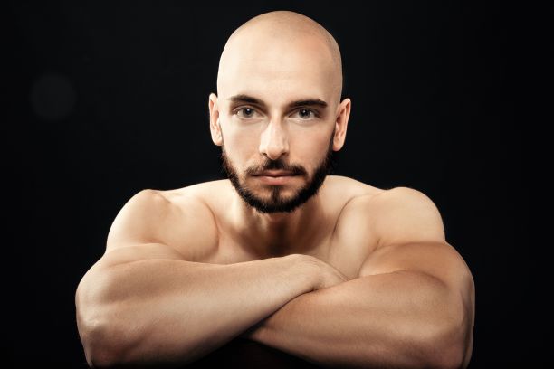 肖像肌肉光头男子坐在交叉双臂，看着严肃的相机图片下载
