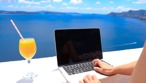 数字游牧民自由职业者女子日光浴与明亮的风景如画的地中海，伊亚-圣托里尼岛，希腊图片下载