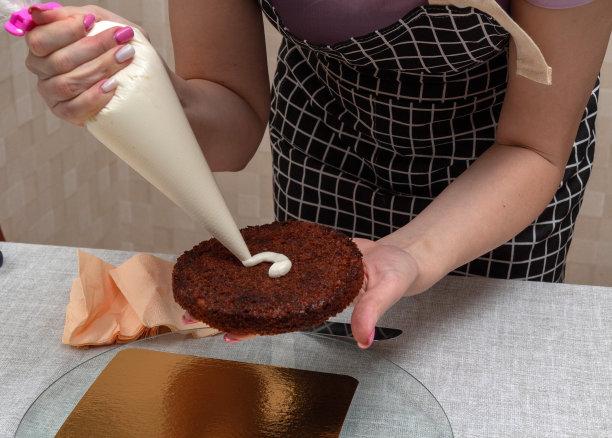 一只手拿着饼干，另一只手拿着糕点袋把奶油挤到蛋糕上。有选择性的重点。图片是关于食品、糖果商的文章。图片下载