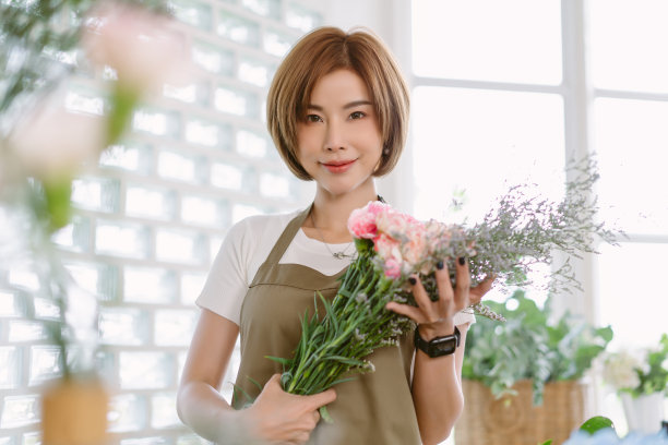 美丽的花店企业家。穿着围裙站在花店的创业小企业主。快乐的亚洲女人拿着花，看着相机。花店，本地，小型商业概念。图片下载