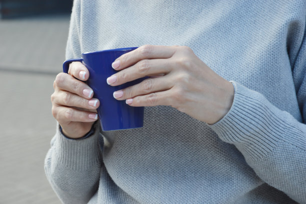 一个穿灰色毛衣的女人手里拿着一杯蓝色的茶或咖啡。图片下载