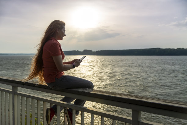 河岸上的一位中年妇女使用笔记本电脑或手机。图片下载