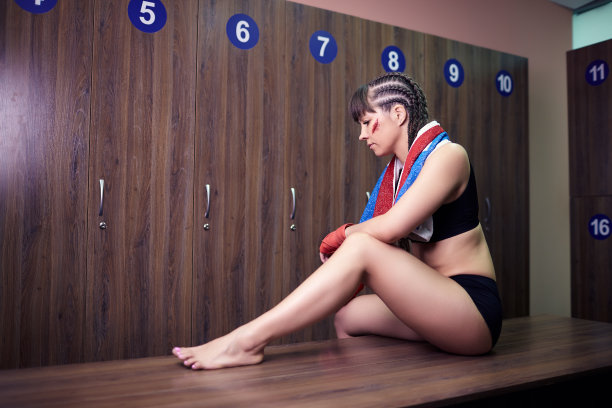 一名手上绑着绷带的女拳击手坐在更衣室的长凳上。图片下载