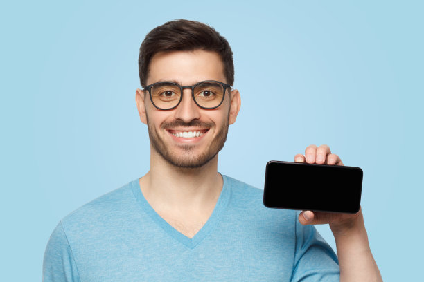 穿着蓝色t恤的年轻人以水平姿势拿着空白屏幕的手机图片下载