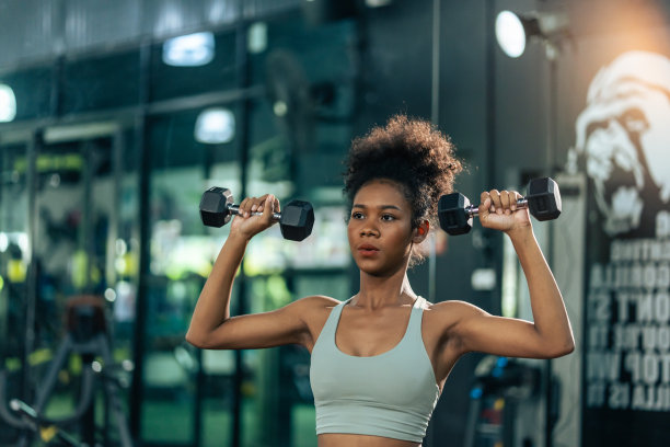 年轻美丽的非裔美国女运动员在体育馆锻炼。有吸引力的积极运动员女孩在运动服锻炼举重哑铃建立肌肉保健和健身。图片下载