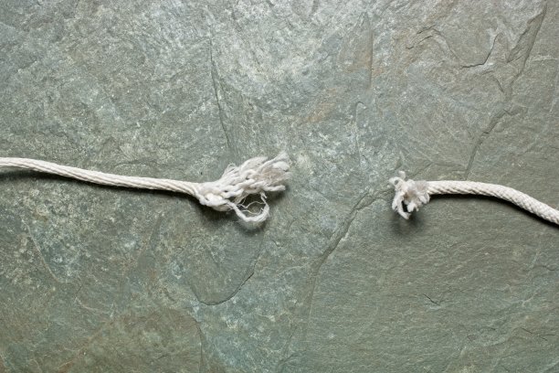 紧张的概念与磨损的两端折断的白色编织绳挂在岩石表面图片下载