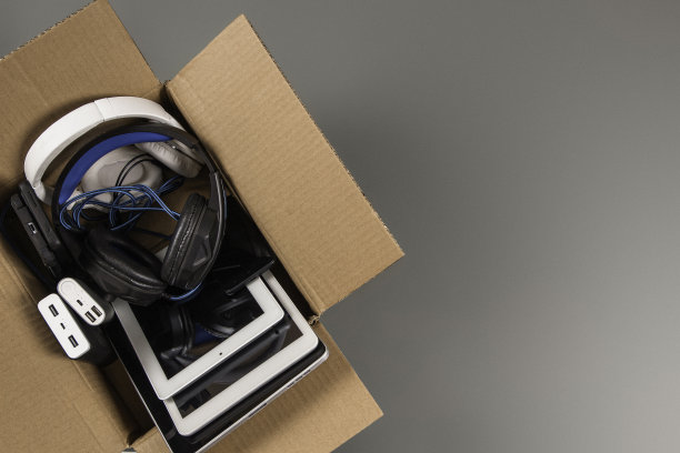 纸箱里装满了旧电脑、平板电脑、智能手机、可回收的电子产品，背景是灰色的。捐赠，电子垃圾，电子垃圾再利用，翻新，回收概念图片下载