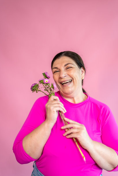 一个成熟的女人在粉红色的背景上拿着一些花的肖像图片下载