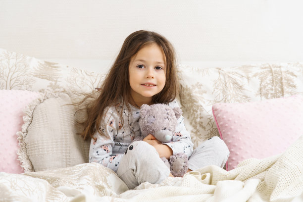 小女孩微笑，睡眼惺忪，抱着最喜欢的毛绒玩具。躺在舒适的床上，清晨醒来。图片下载