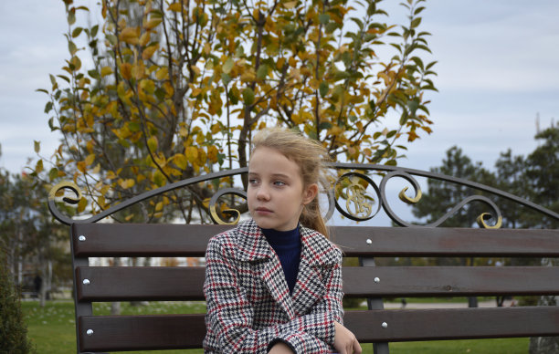 一个穿着格子大衣的漂亮女孩在公园里散步时坐在长凳上图片下载