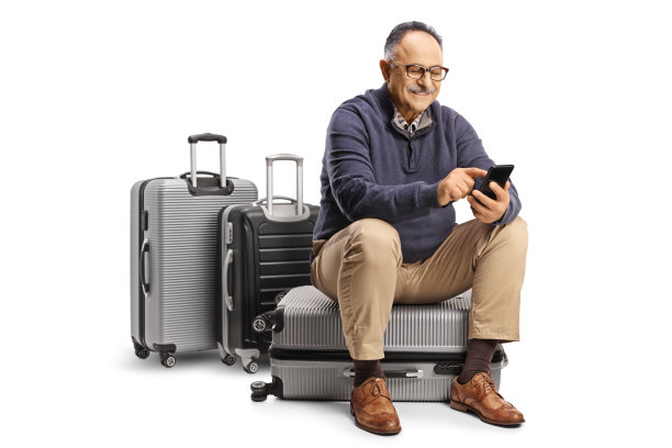 年长的男旅客坐在行李箱上使用智能手机图片下载