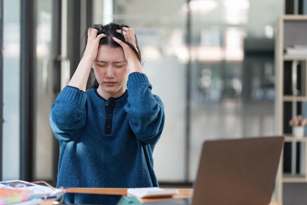患有办公室综合症的亚洲年轻职场女性在长时间使用笔记本电脑工作后，会感到头痛和背部压力过大。医疗保健，办公室综合症概念图片下载