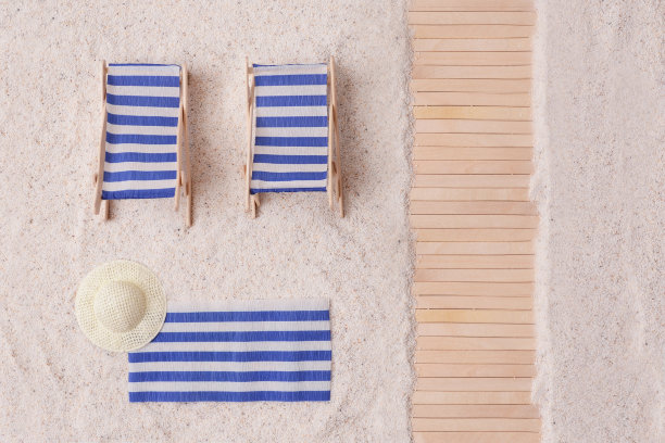 沙滩上有一条铺着蓝白条纹毛巾、躺椅和草帽的木制小径。海滩上的热带夏日。假期的最小概念。图片下载