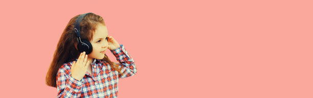 小女孩的肖像，戴着耳机，在粉红色的背景上听音乐图片下载