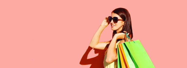 美丽的黑发年轻女子与粉红色背景彩色购物袋的肖像图片下载