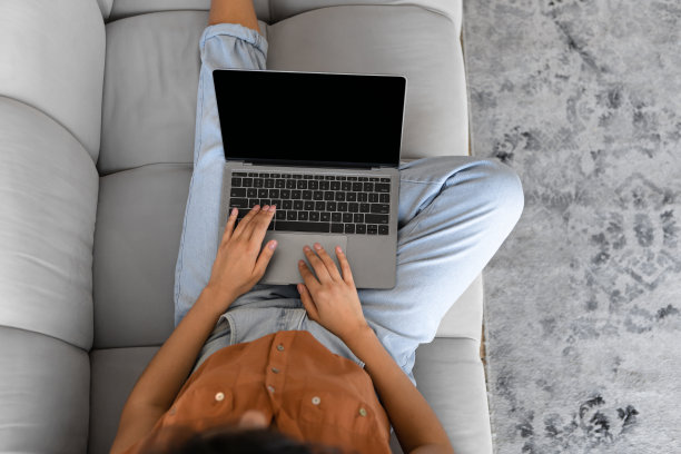 年轻女子坐在沙发上，在家里使用空屏幕的笔记本电脑的俯视图，网站设计的模型图片下载