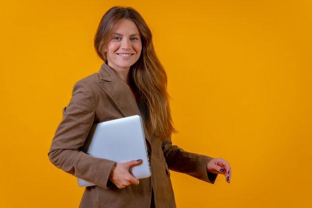 一位女商人的肖像，黄色背景上有一台电脑，年轻的企业家概念图片下载