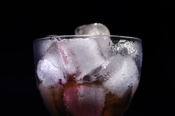 在霓虹灯的黑色背景下，一个装有冰块和饮料的透明玻璃杯。鸡尾酒，派对和夜生活的概念。图片下载