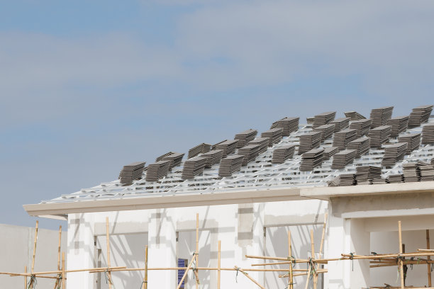 屋顶瓷砖以包形式排列在屋顶金属板条上。在木板屋顶上铺设瓦片的准备工作。正在施工的屋顶，屋顶瓦片堆叠，竹脚手架。图片下载