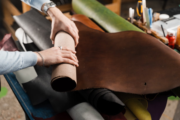 皮革工匠正在车间里触摸真皮卷。皮具车间不同颜色的真皮卷。图片下载